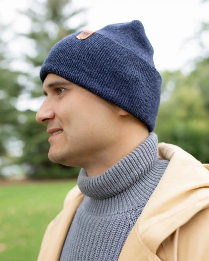 Denim blue beanie with turned cuff and tan logo patch, side view