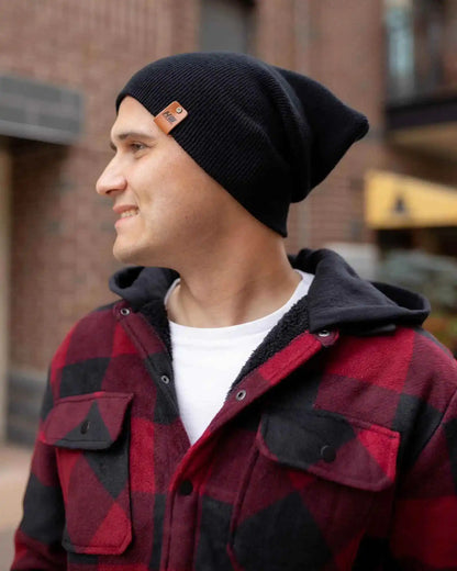 Midnight black cuffed knit beanie with orange logo patch, angled view.