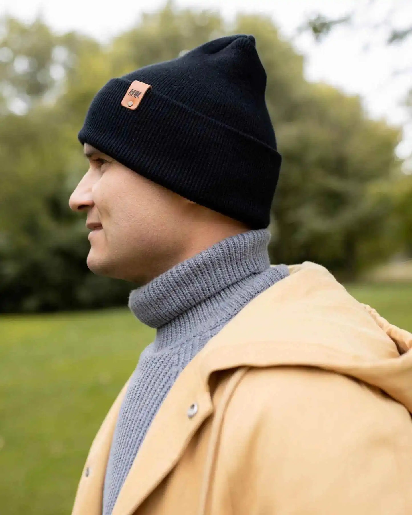 Midnight black knit beanie with orange logo patch on top edge.