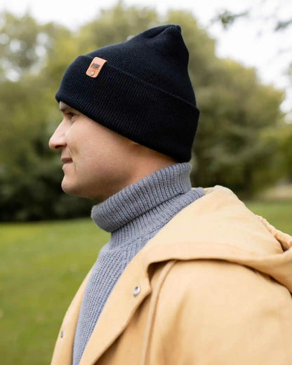 Midnight black knit beanie with orange logo patch on top edge.