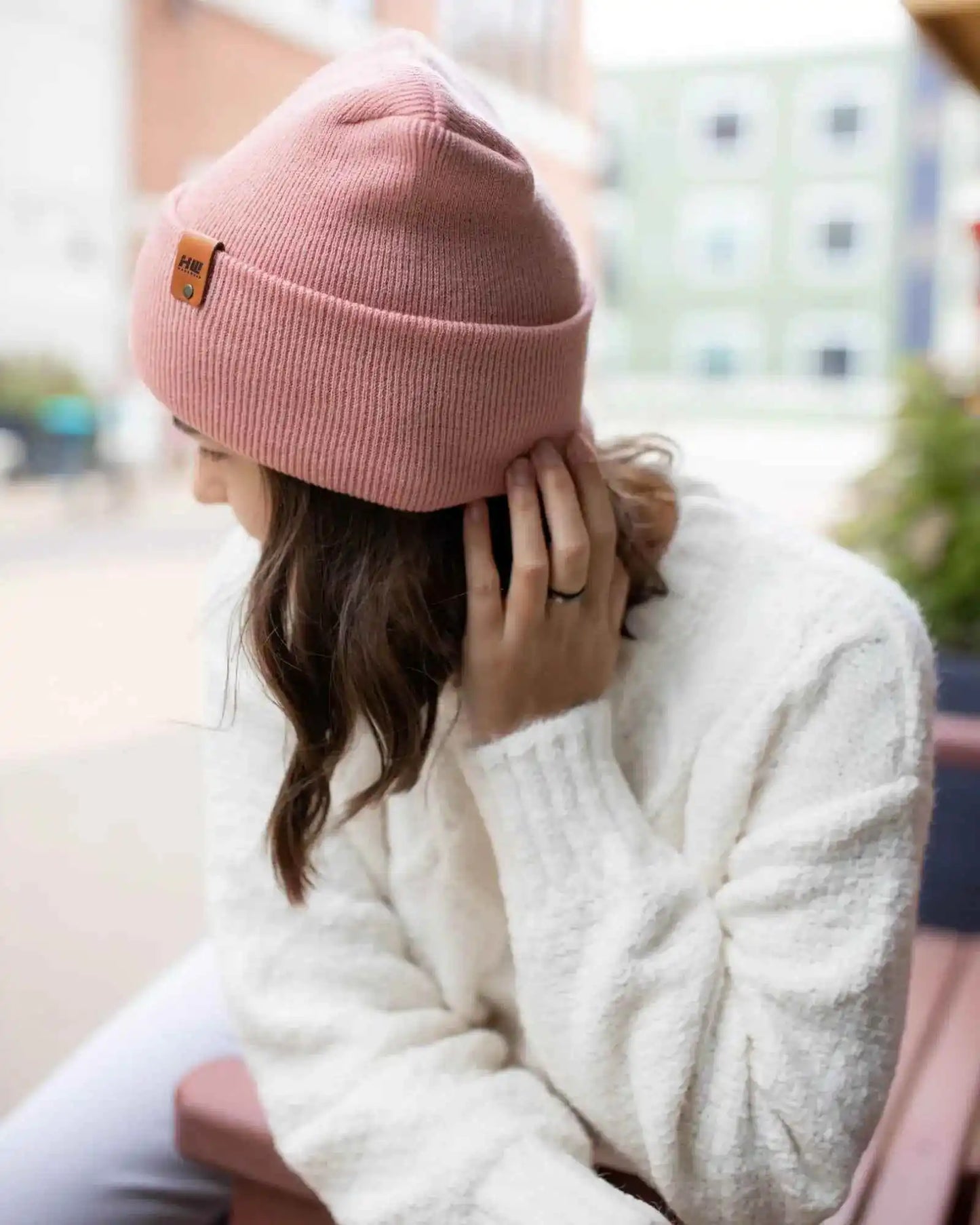 Pearl pink knit beanie with square logo patch, worn and viewed from side
