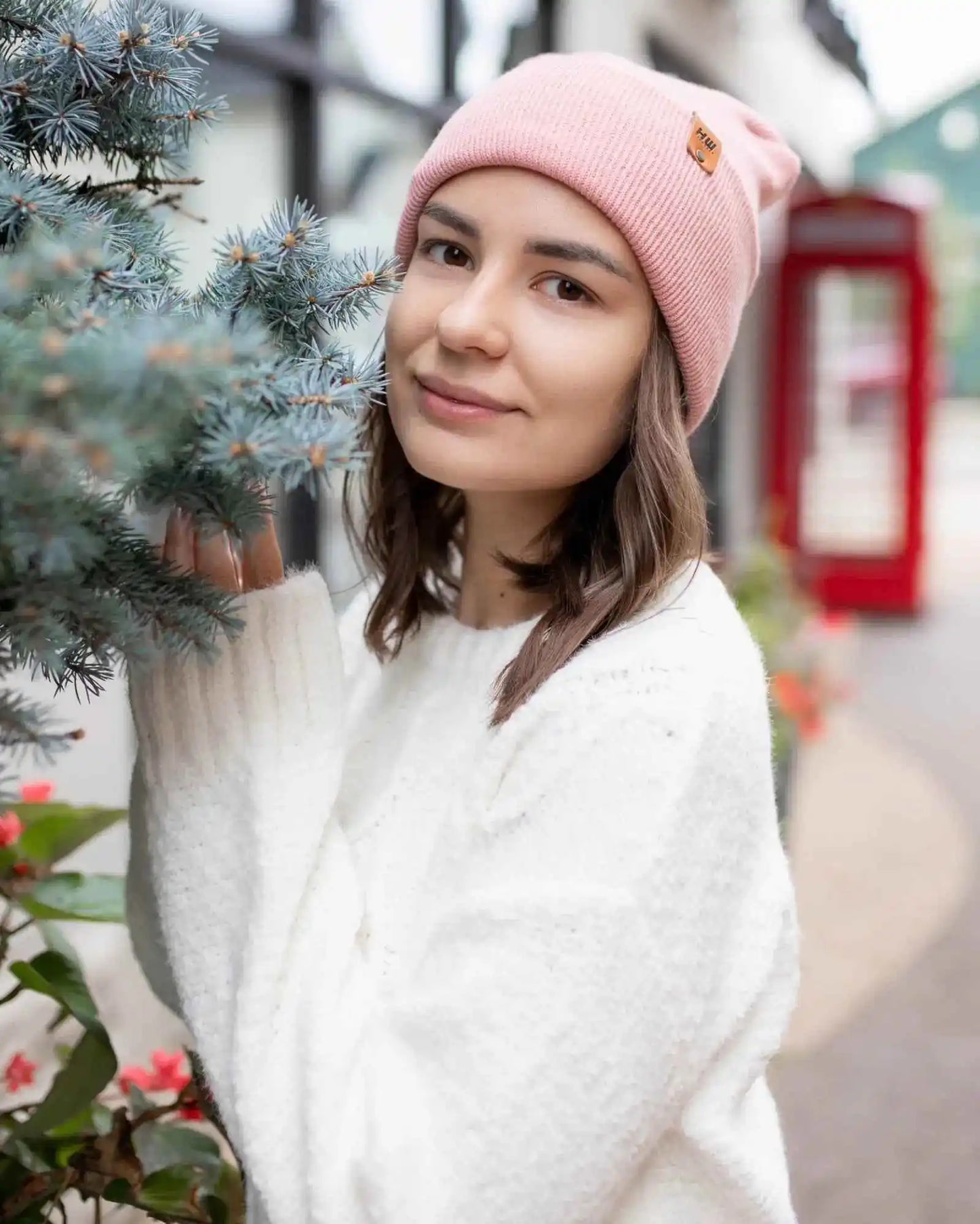 Pearl pink knit beanie with square logo patch, worn and viewed from front