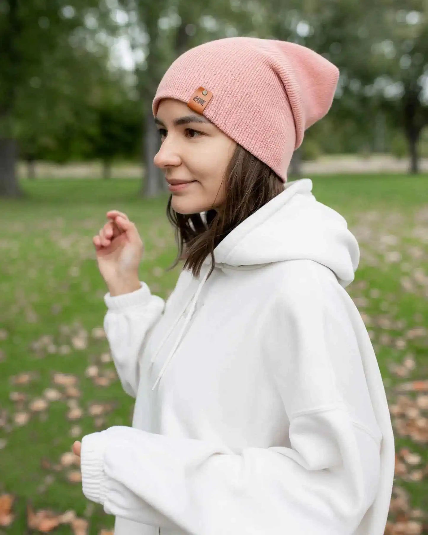 Pearl pink cuffed beanie with small square logo patch, worn on head in profile
