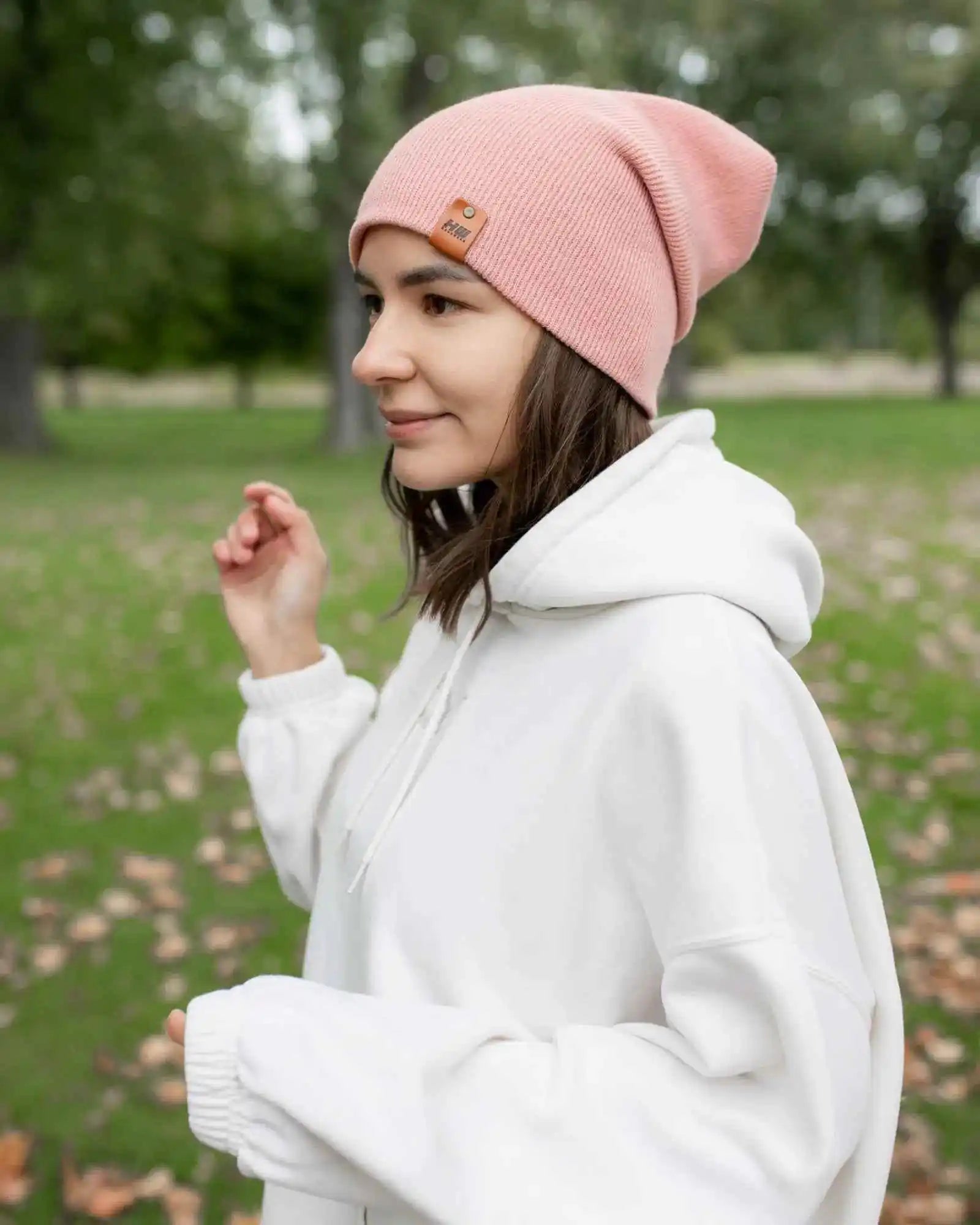 Pearl pink cuffed beanie with small square logo patch, worn on head in profile