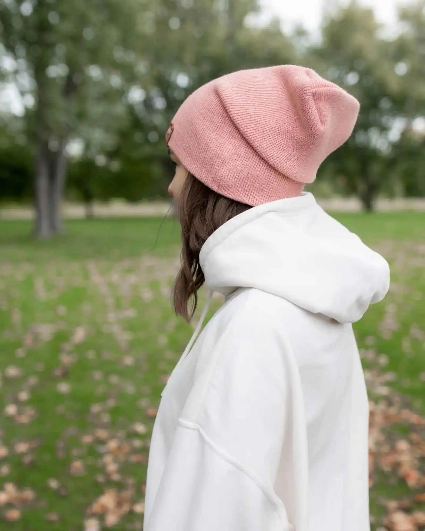 Pearl pink beanie with cuff and small square logo patch, worn from back