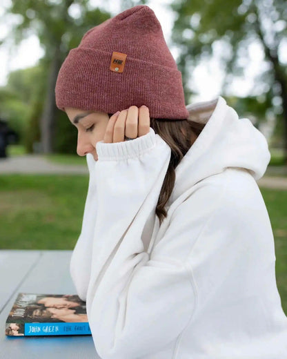 Rusty burgundy knit beanie with square logo patch, worn under a white hoodie