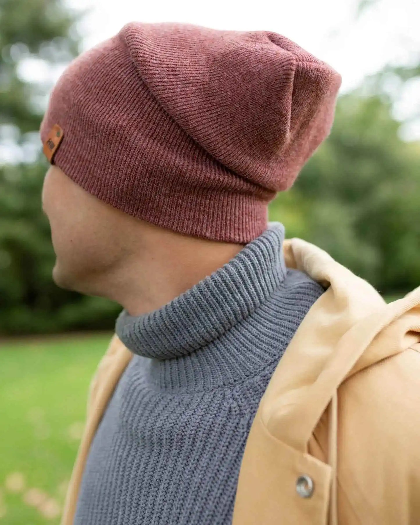 Rusty burgundy knit beanie viewed from side with logo patch on cuff