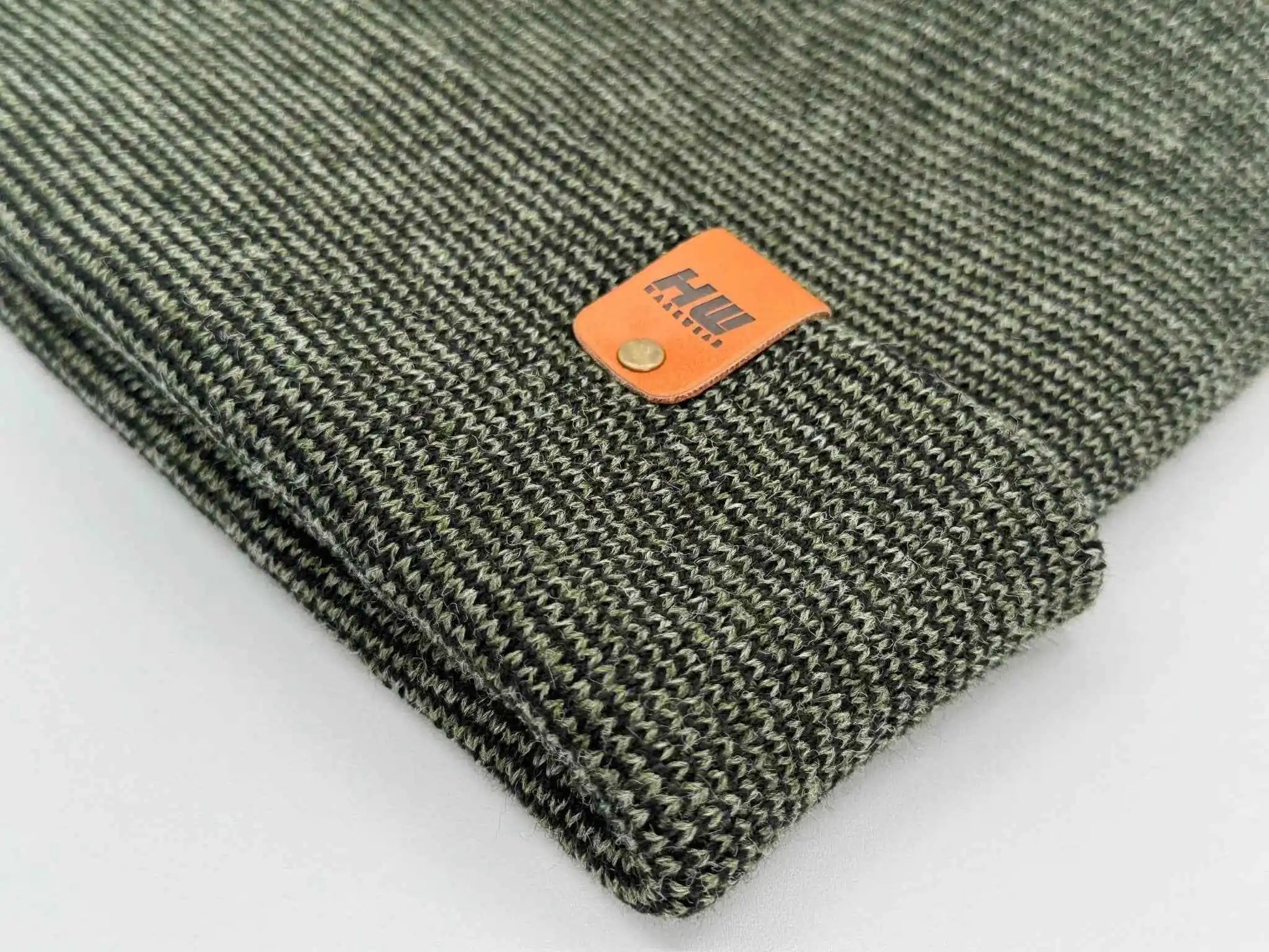 Dark green knitted beanie cuff with orange brand patch on textured fabric