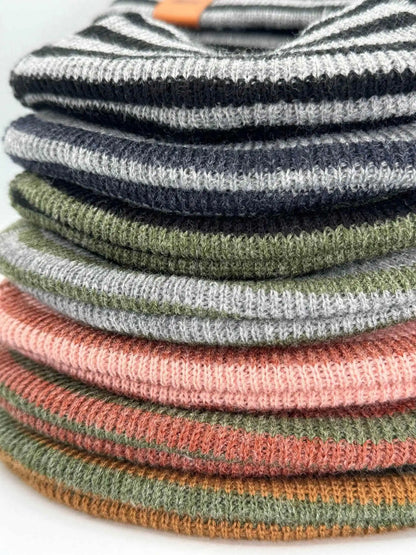 Stack of striped knit beanies with folded cuffs and brand tags in mixed colors