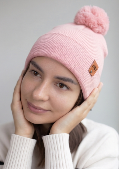 Pearl pink ribbed knit beanie with folded cuff, pom pom, and logo patch