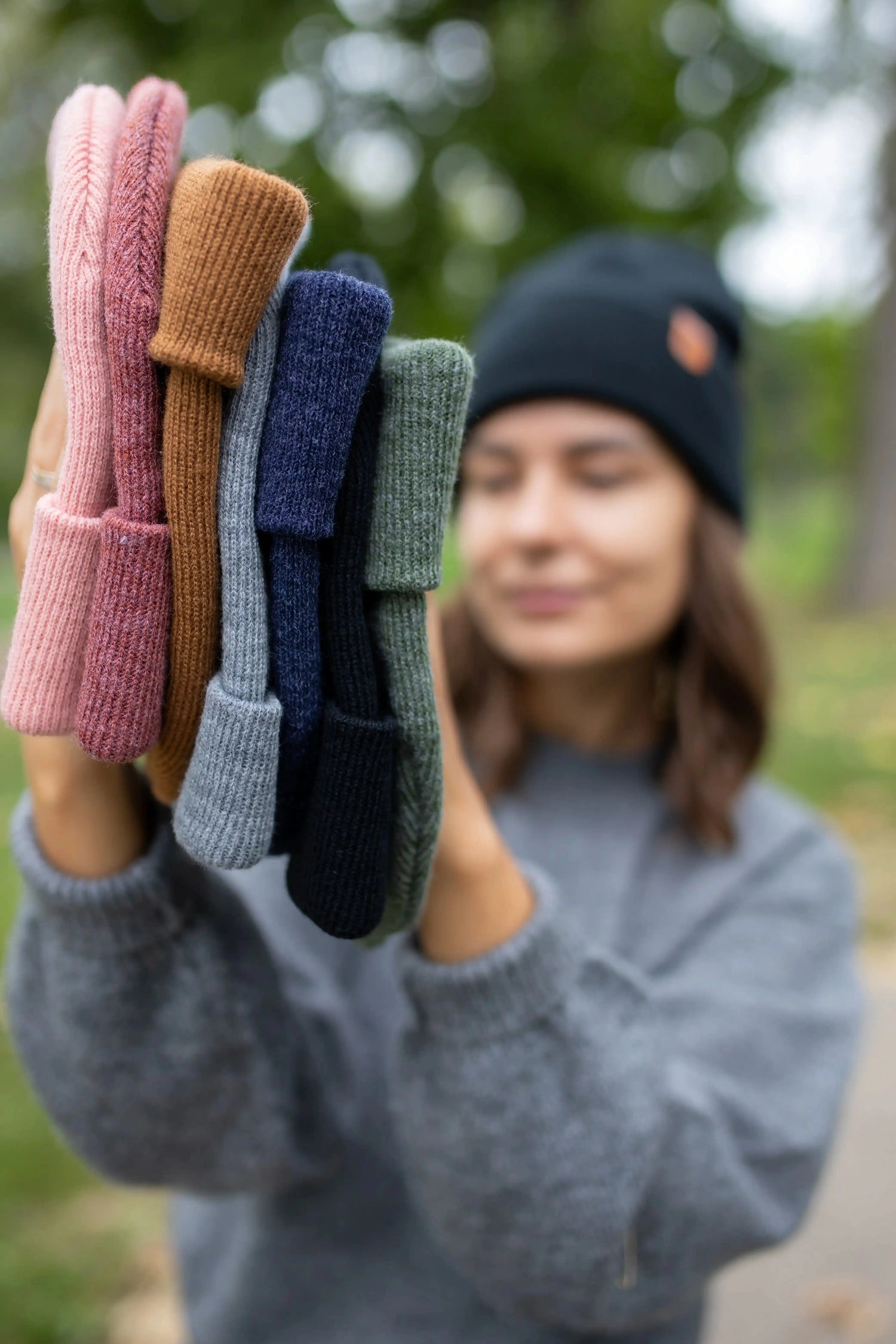 Person holding a stack of colorful knit hats outdoors
