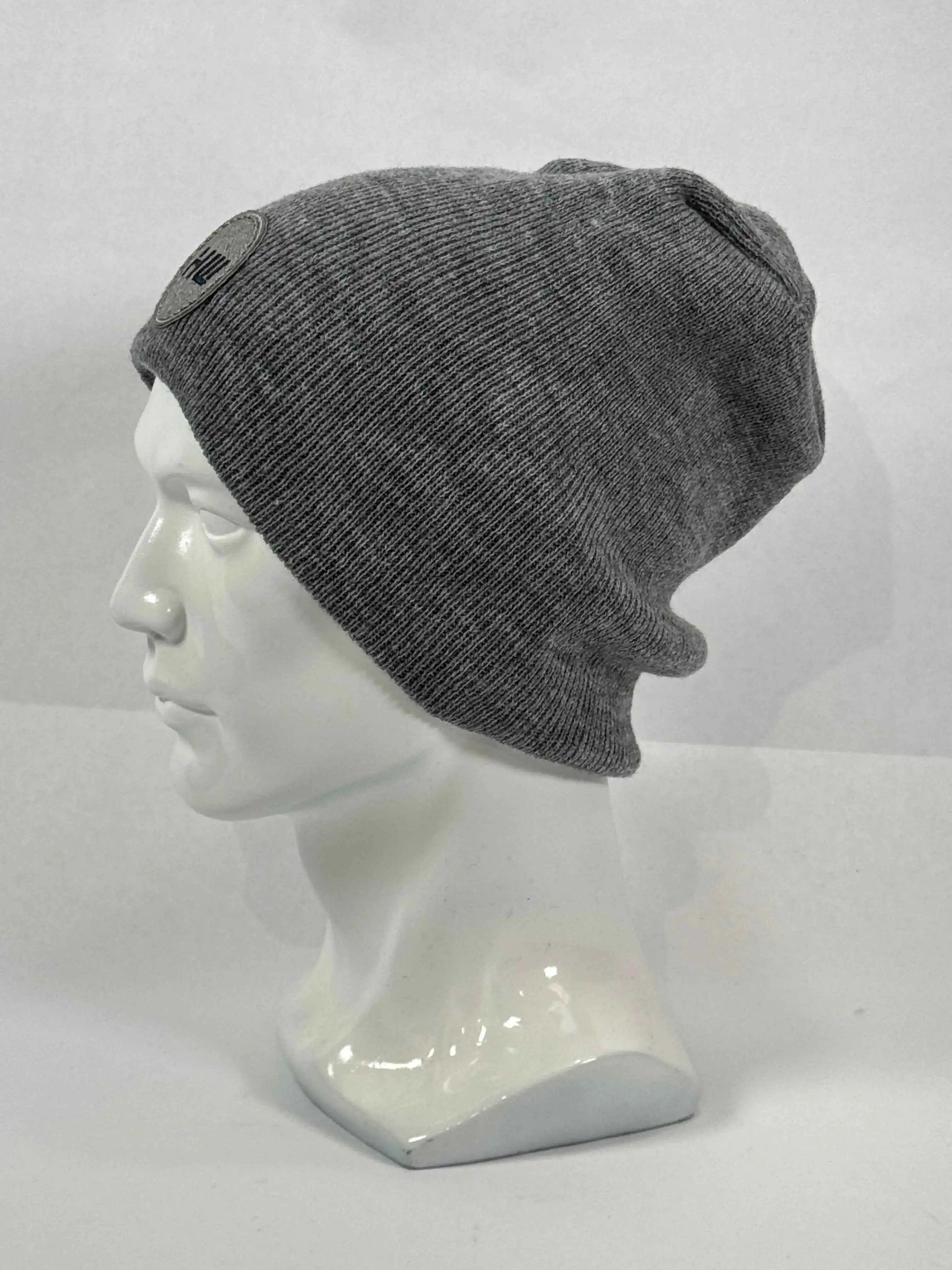Gray knit beanie on mannequin, uncuffed with ribbed texture and side logo patch