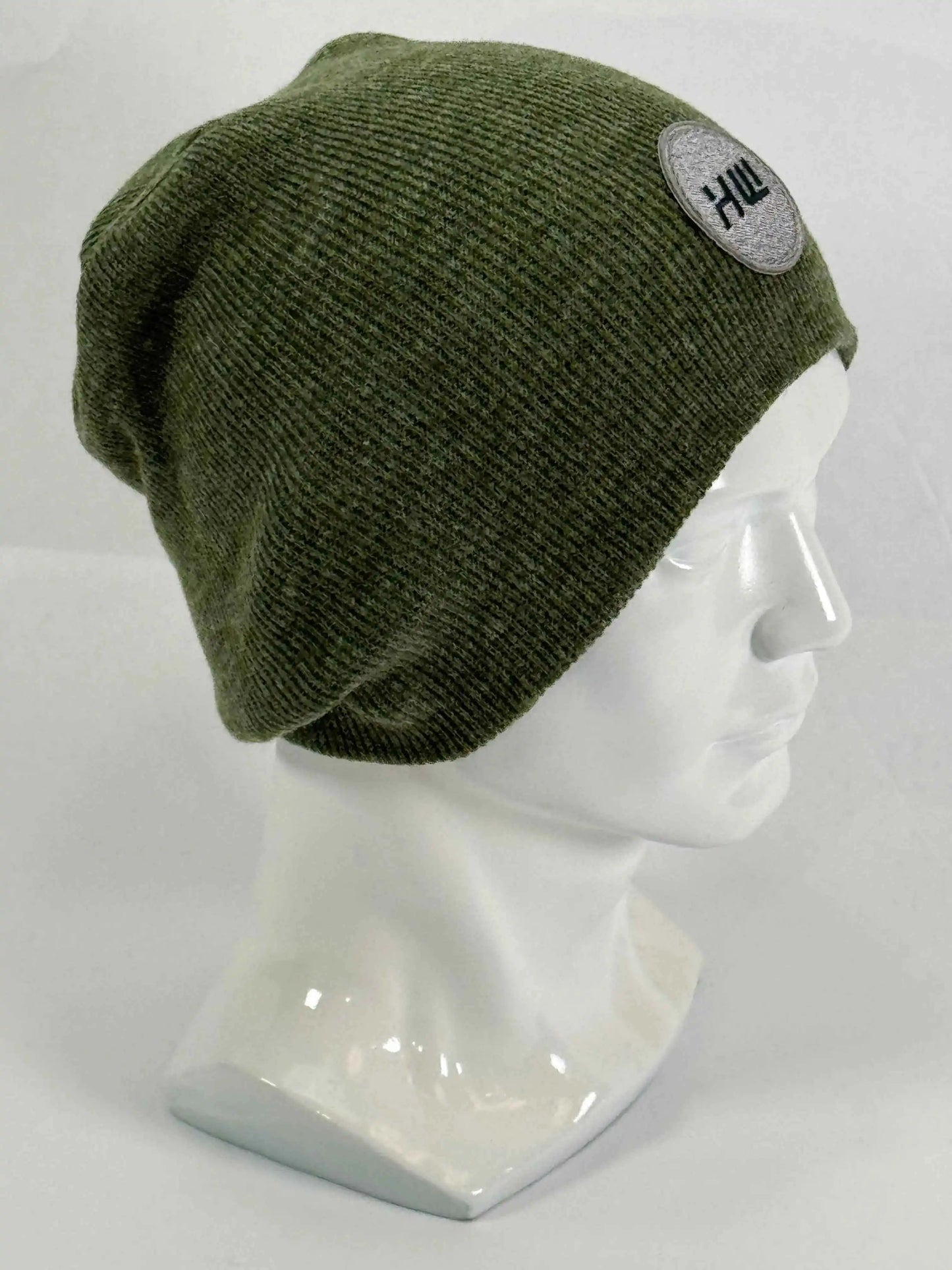 Olive green knit beanie with un-cuffed rolled edge and round HUI logo patch.