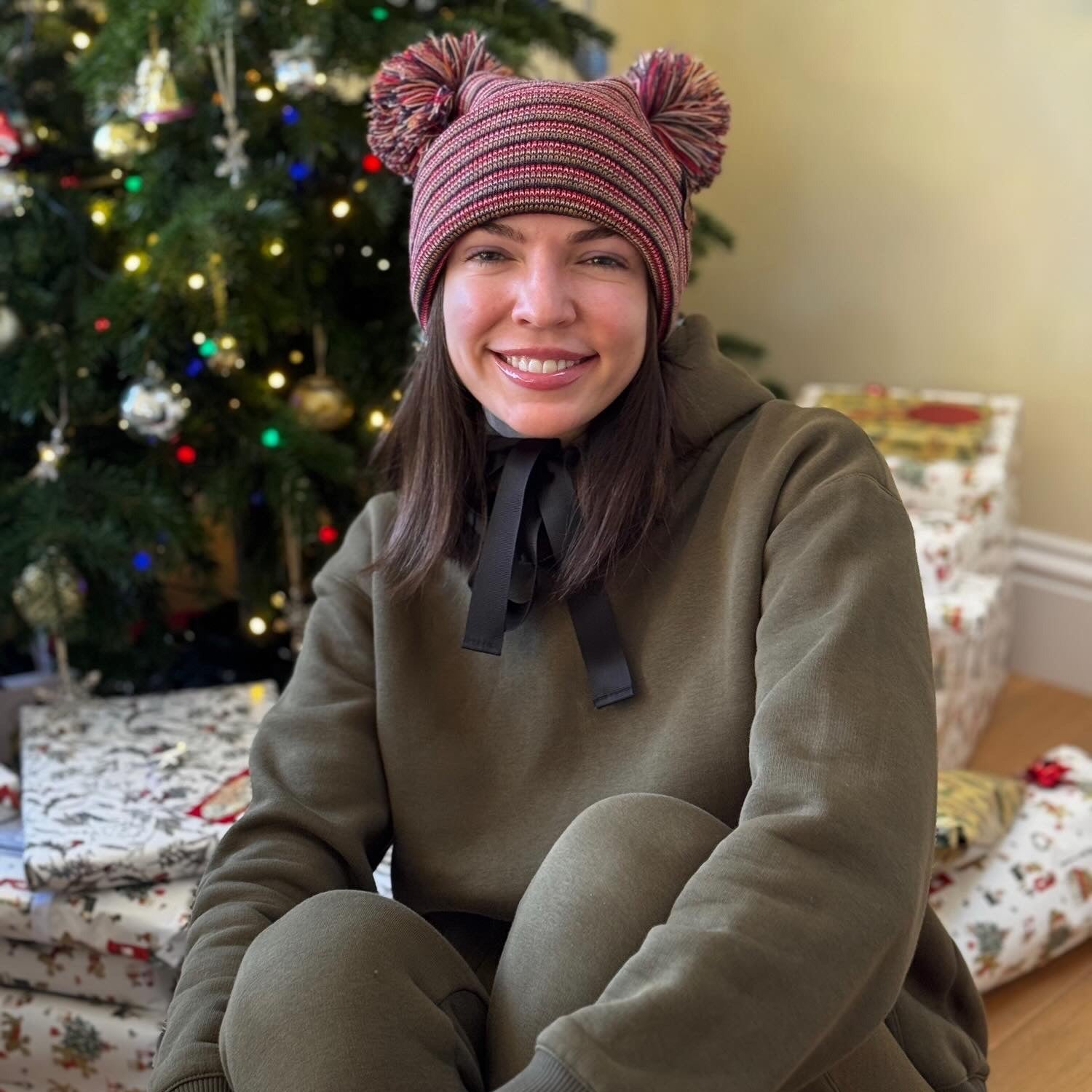 Person wearing a festive knit hat sitting in front of a decorated Christmas tree. 