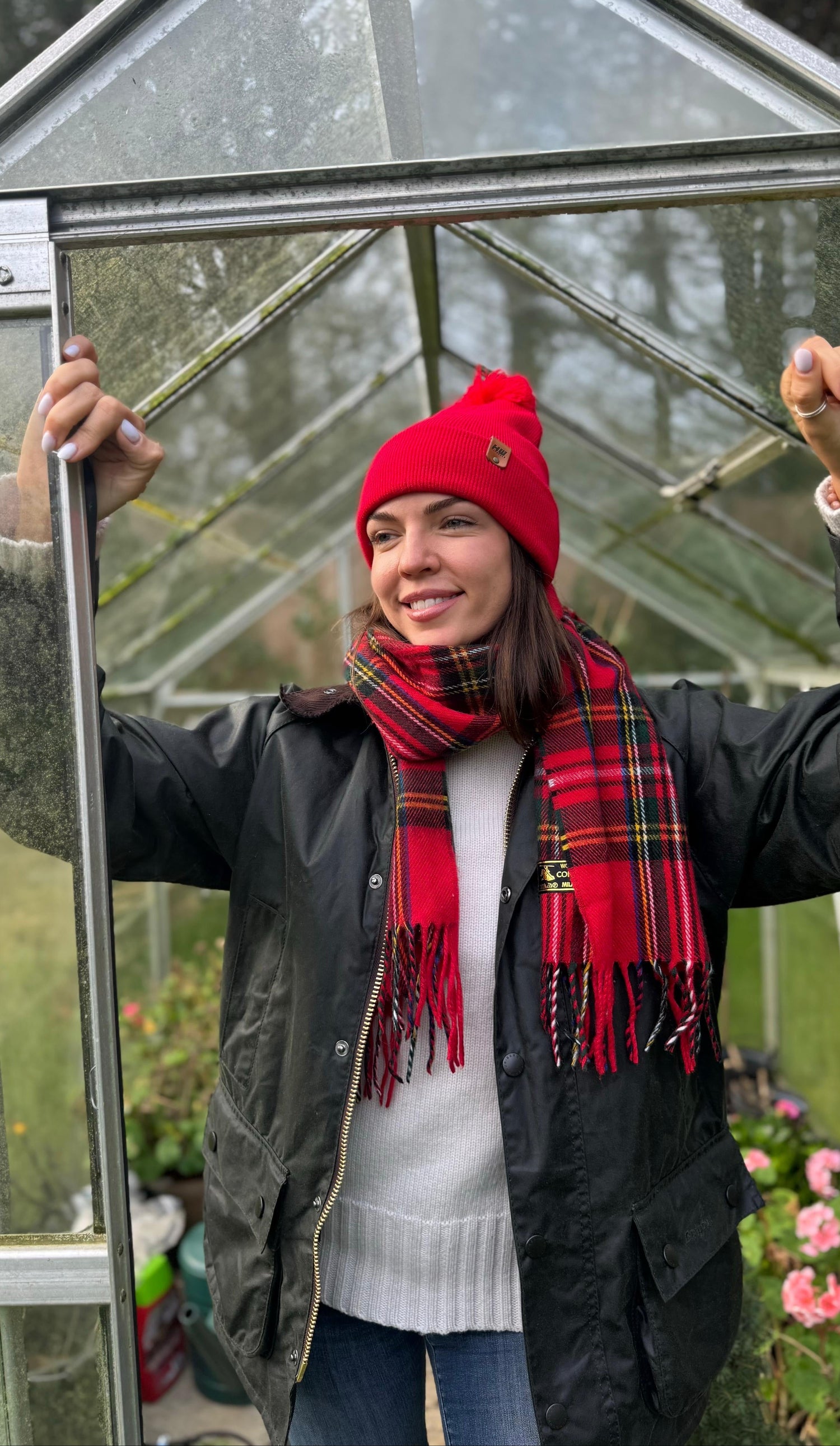 Person wearing a red beanie and scarf standing inside a greenhouse