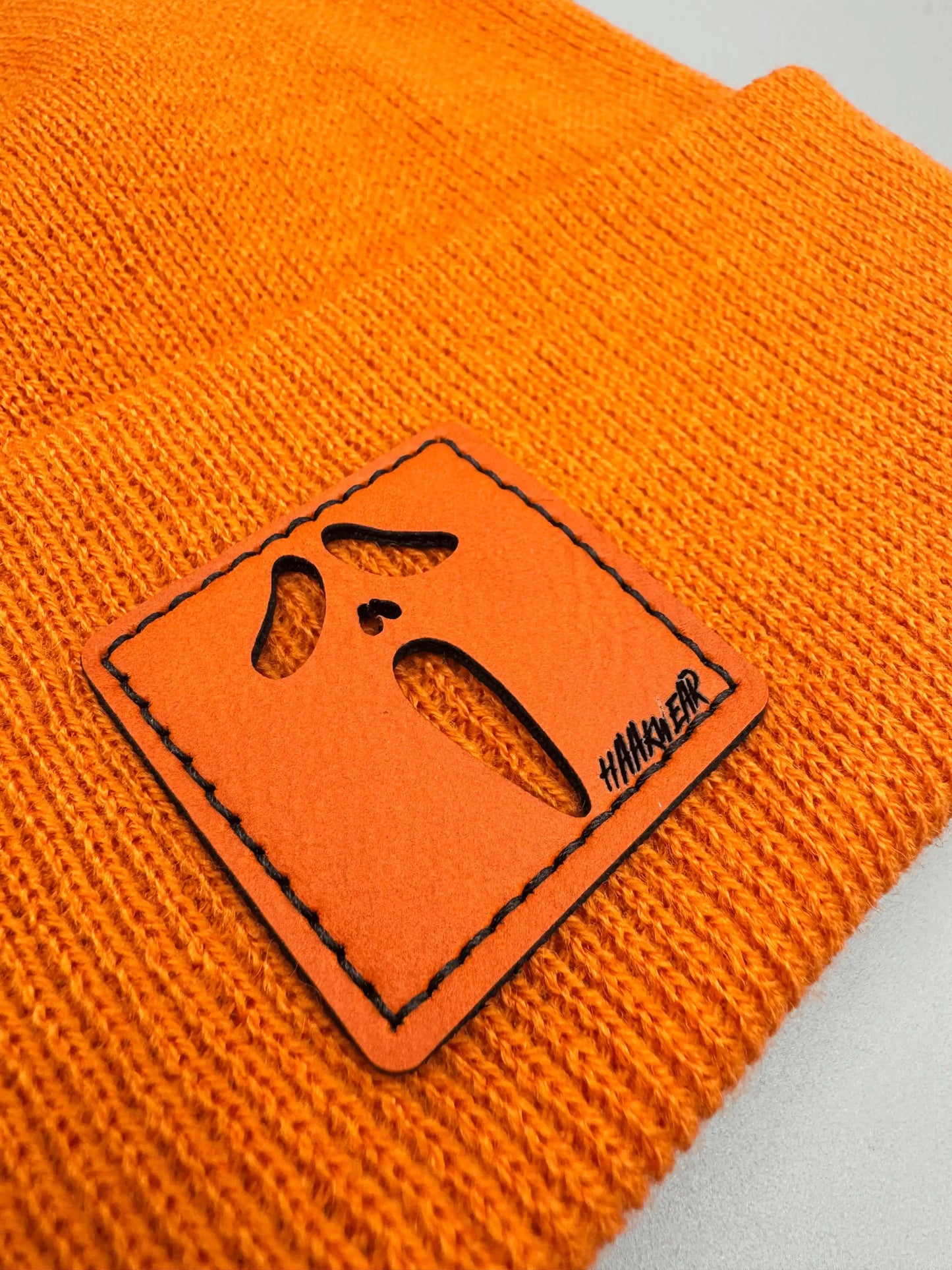 Orange knit beanie detail: orange/black rectangular character patch on cuff