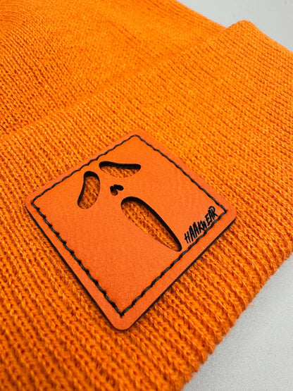 Orange knit beanie detail: orange/black rectangular character patch on cuff